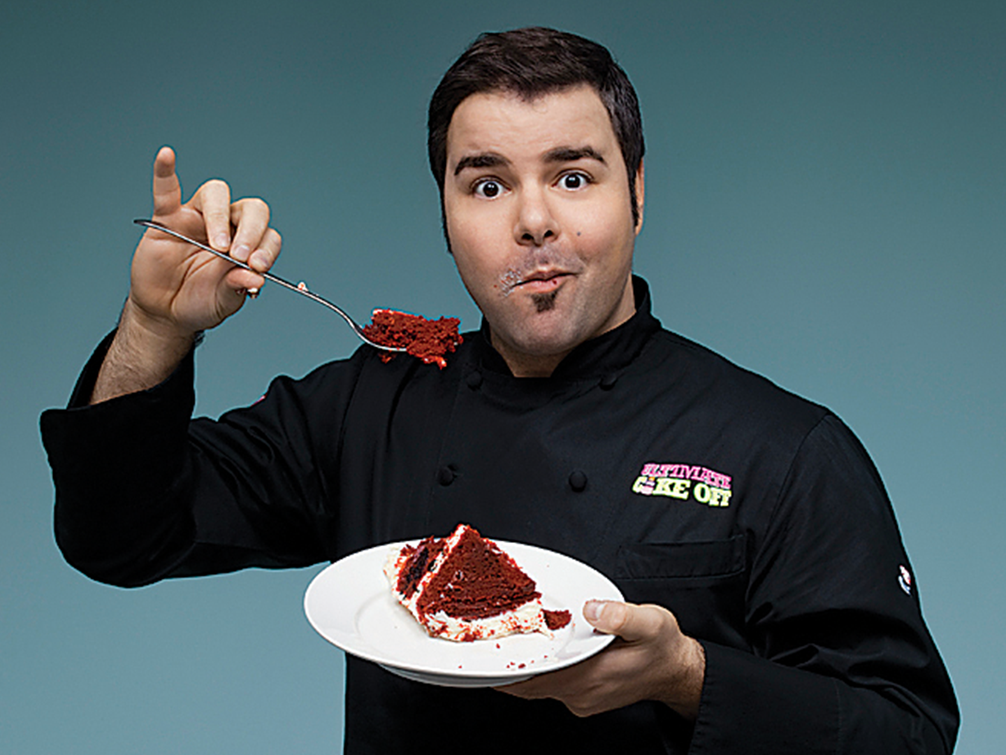 A chef wearing black suite and eating a cake.