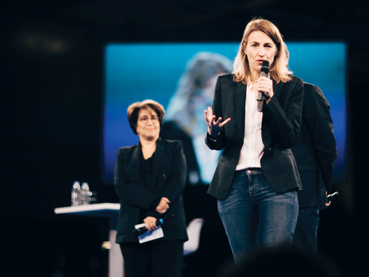 A woman stands and addresses the audience during a speech.