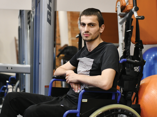 Young solider, in physical rehabilitation, sitting in a wheel chair with exercise equipment all around him.