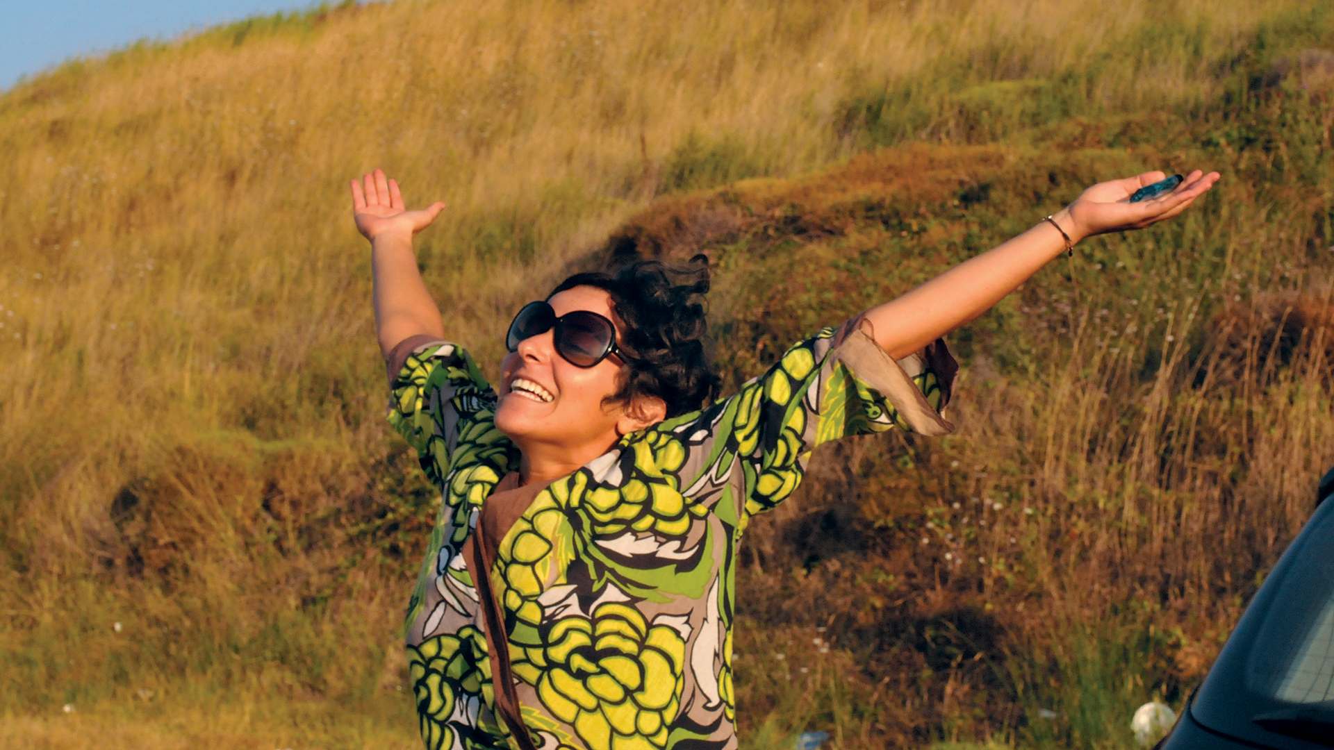 A girl with sunglasses and opened hands to the sky in the nature