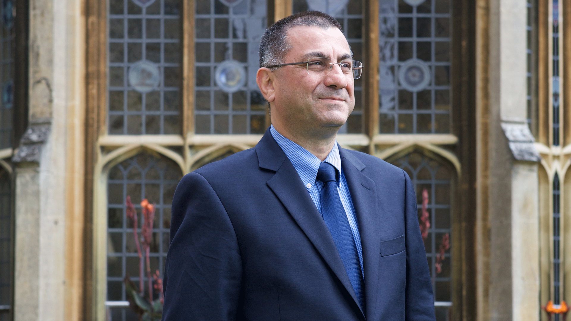 University professor with glasses and blue suit poses in front of a campus building at University of Oxford