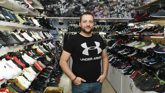 A man standing with his hands in his pockets in between rows of sneakers from floor to ceiling. 