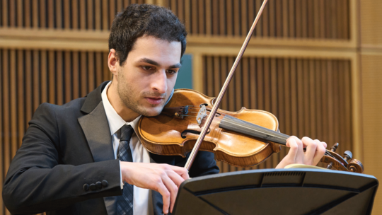 Male musician plays the violin in a concert room