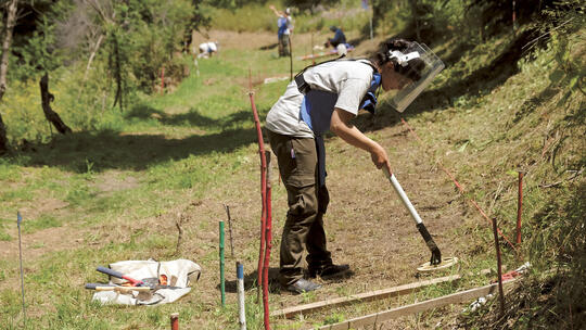 A deminer scans the ground with a metal detector.